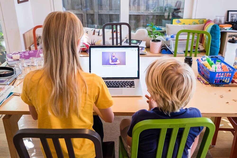 two primary school aged children engaged in home schooling using remote learning pack on laptop