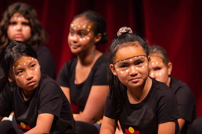 group of primary school students with First Nations face make-up waiting to perform their indigenous dance in concert.