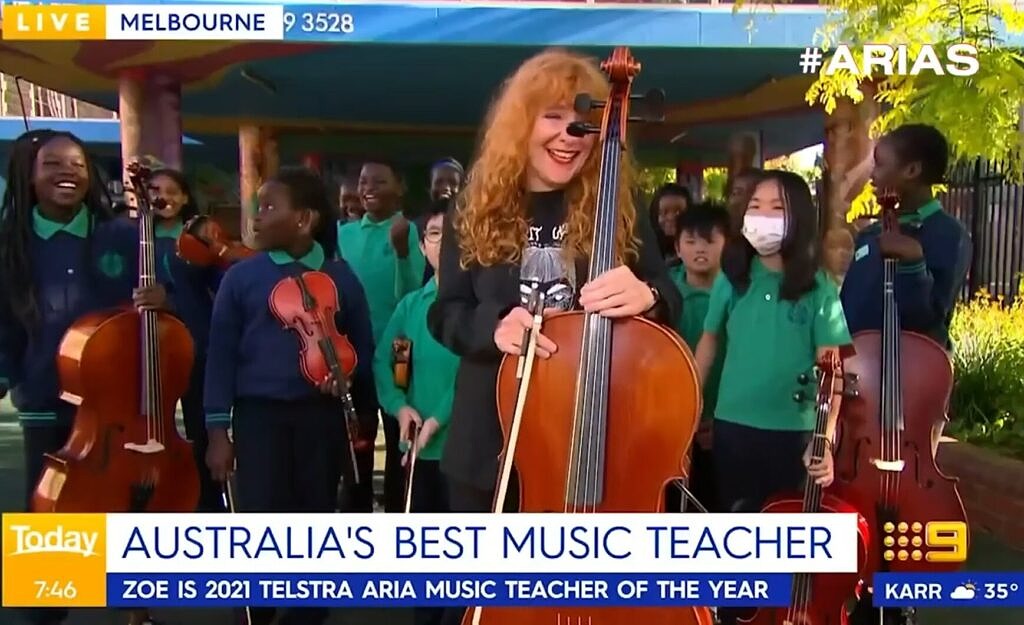 Teaching Artist Zoe Barry holding cello smiling, surrounded by primary school students. Today TV show caption says Australia's Best Music Teacher