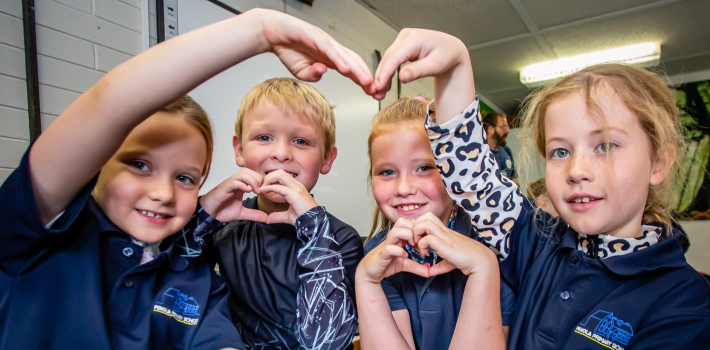 four smiling primary school students make heart signs with their hands 