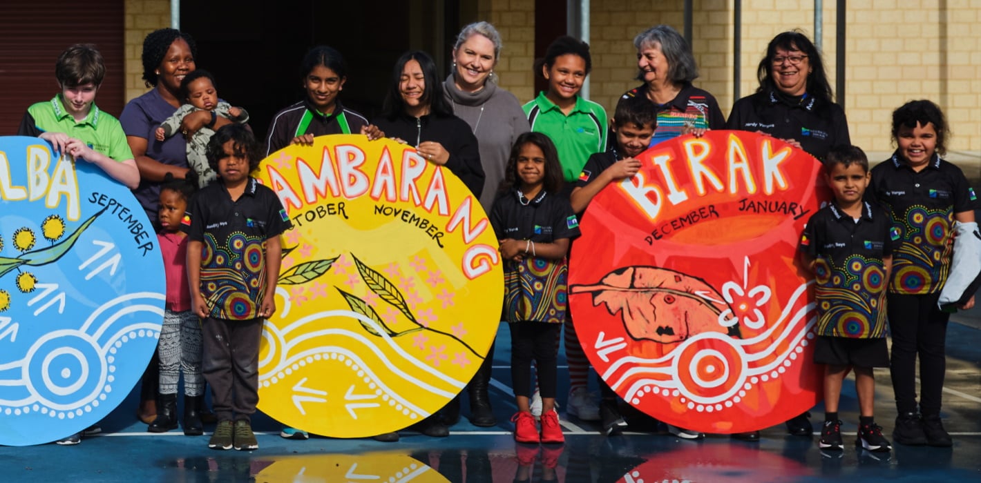 Teachers and primary school students stand proudly next to indigenous designed signs they made in arts lesson visual arts lesson on First Nations