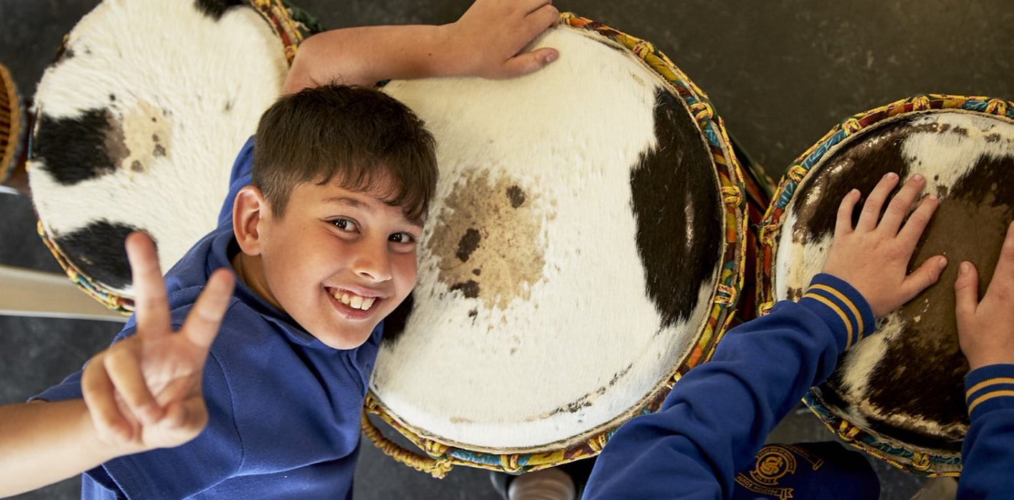 Primary school student playing drum giving victory hand sign