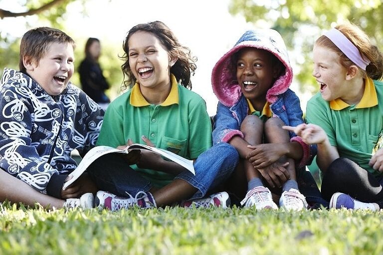four primary school students enjoy reading books outside on the lawn