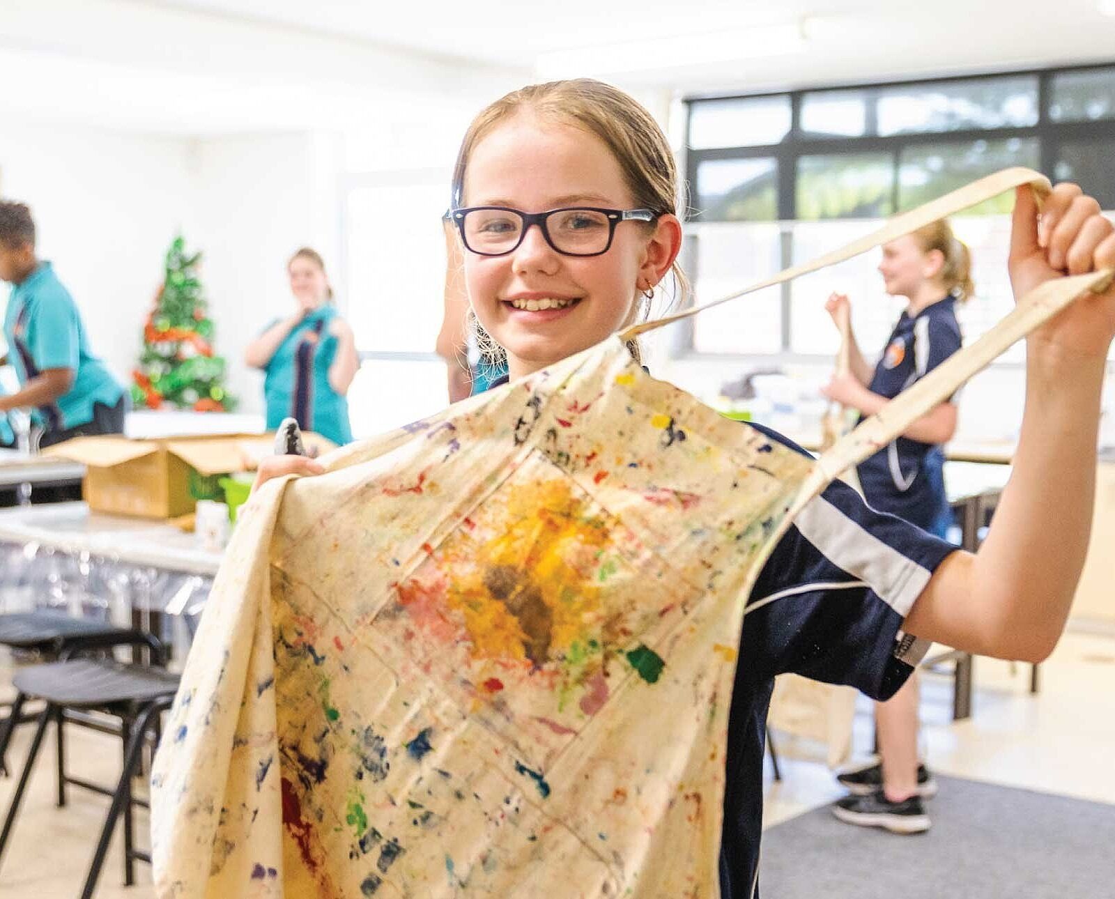 A female student holding up her art apron during a visual arts lesson in the Song Room program.