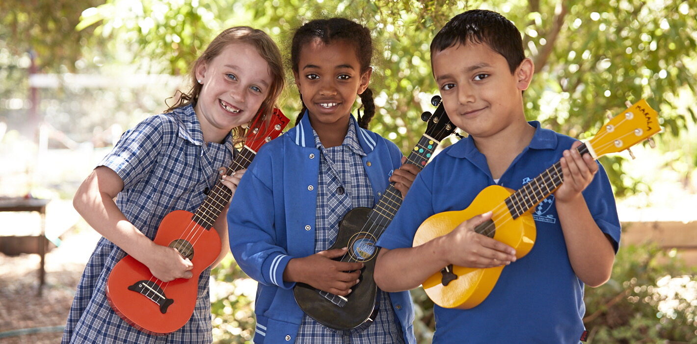 three primary school students enjoying arts learning lesson on ukuleles