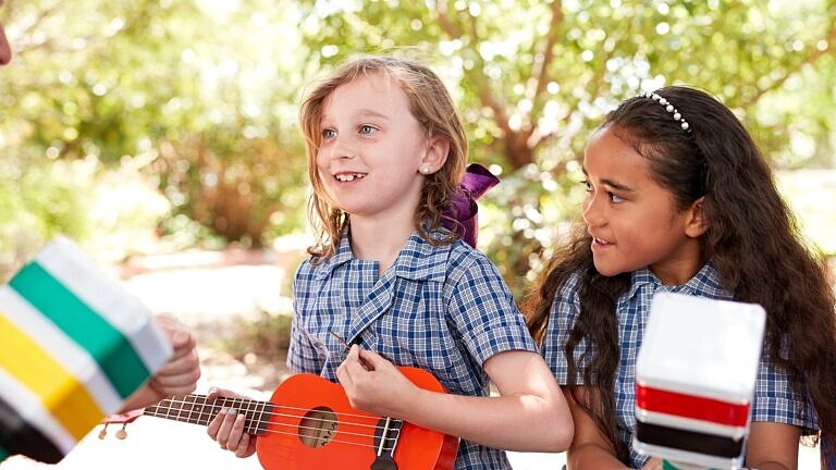 two primary school students engaged in arts learning outdoor music class playing musical instruments