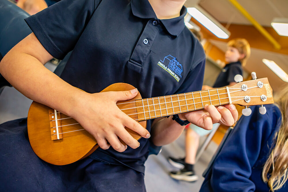 Primary school student playing ukulele in arts learning music lesson