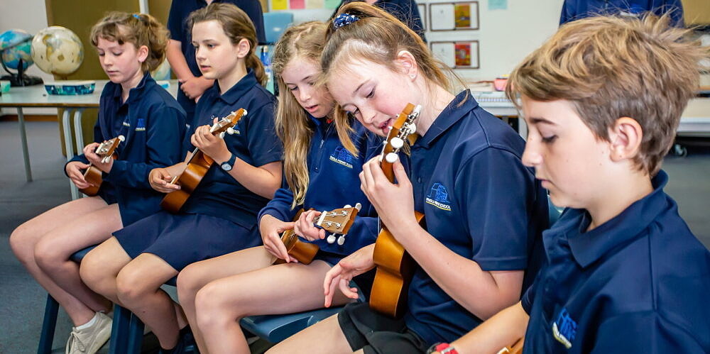 Primary school students playing ukelele in arts learning music lesson